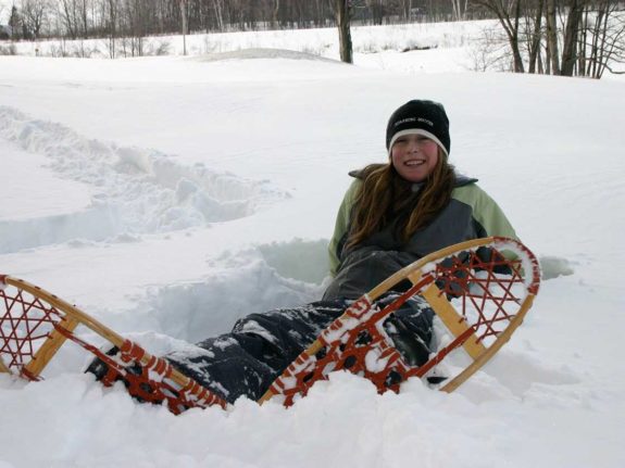 A girl sitting in the snow wearing snowshoes